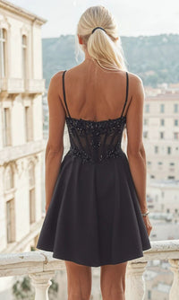 Woman showing the back of a short black dress with beaded details standing on a balcony with a cityscape background