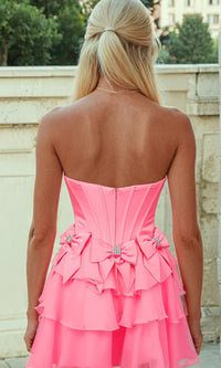 Woman showing the back of a short pink dress with bows, standing outside in front of a concrete wall.