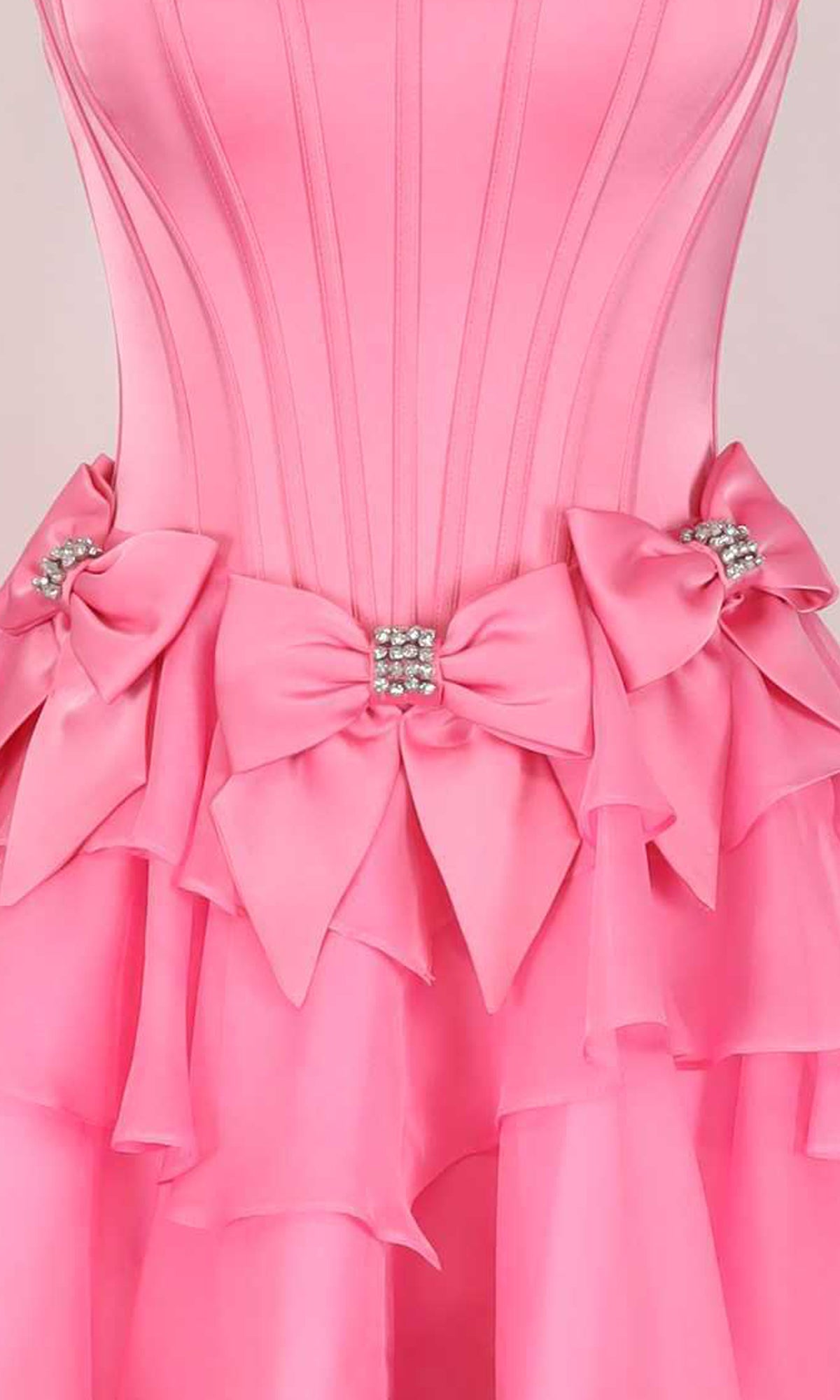Close-up of a pink dress with embellished bows around the waistline on a light background