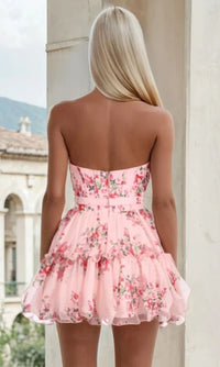 Woman showing the back of a short pink floral dress she's wearing, with a blurred background