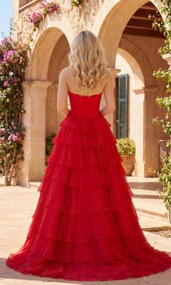 A woman with long blonde hair stands outside, facing away, wearing the A-Line Ruffle Prom Gown: PromGirl Exclusive 250203. A Mediterranean-style building and flowers are visible in the background.