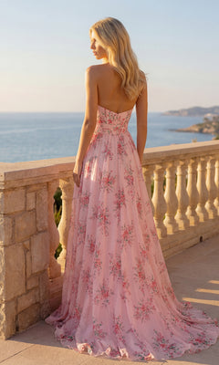 A woman in the PromGirl Exclusive 250236 Floral Chiffon Prom Dress stands on a stone terrace overlooking the ocean and distant coastline at sunset.