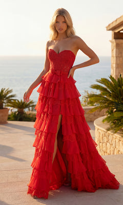 A woman in a red Chiffon and Lace Prom Gown (PromGirl Exclusive 250238) stands outdoors by lush plants and stone architecture, with the ocean in the background.