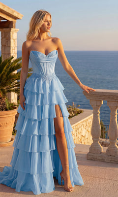 A woman in the light blue Ruffled Long Prom Dress: PromGirl Exclusive 250267 with a high slit and sweetheart neckline stands on a terrace overlooking the ocean, bathed in evening sunlight.