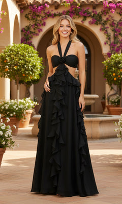 A woman stands outdoors by a fountain, wearing the PromGirl Exclusive 250269 long black prom dress with a halter neckline, ruffle details, and cutout sides; potted plants and flowers are in the background.