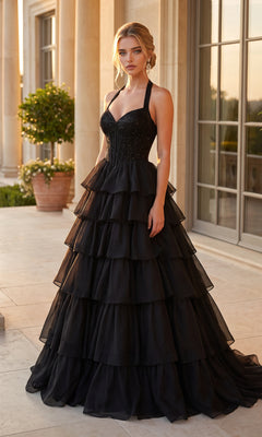 A woman stands outdoors in front of large windows, wearing the PromGirl Exclusive 250352 Halter Prom Ball Gown in black, featuring a fitted corset bodice and a dramatic tiered ruffle skirt.