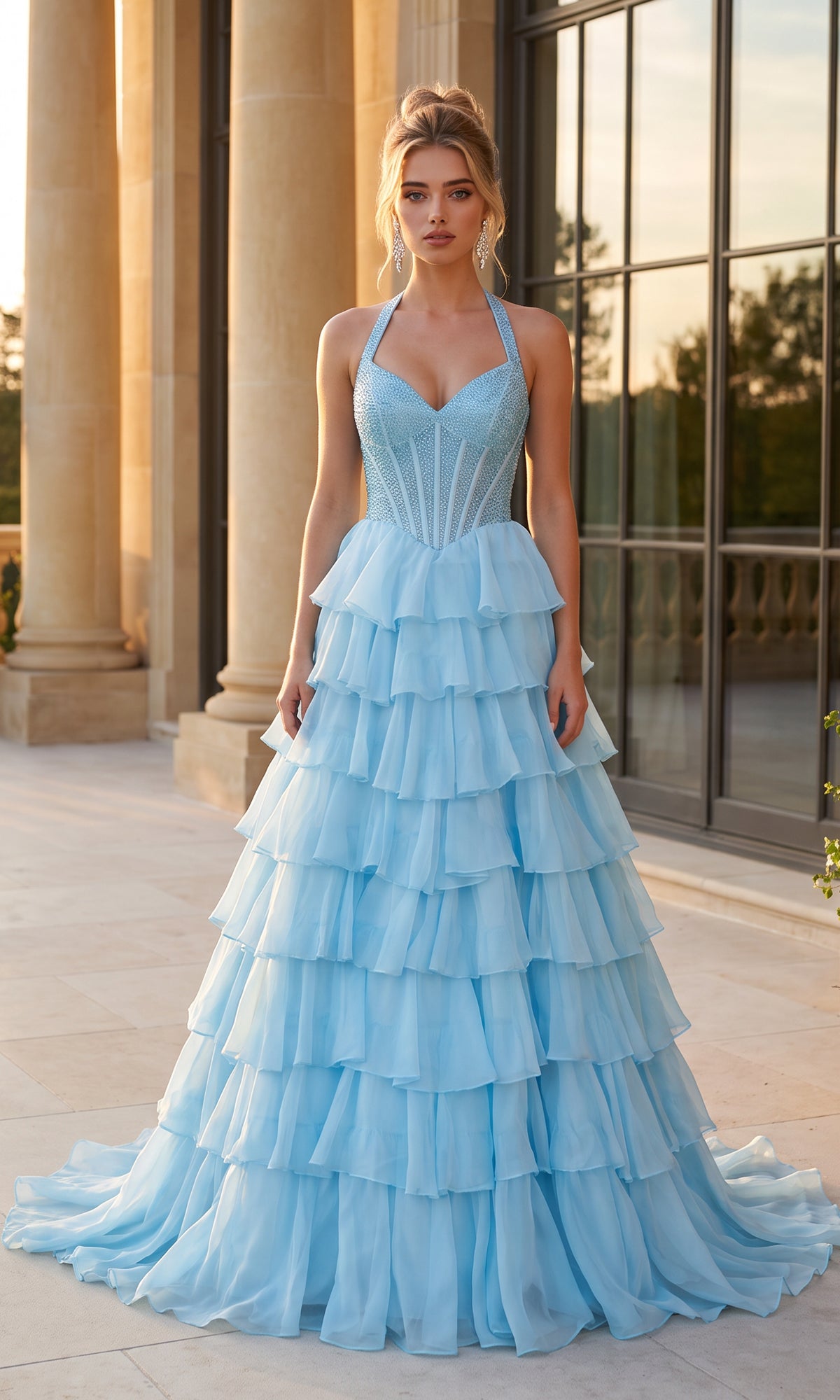 Wearing the PromGirl Exclusive 250352 Halter Prom Ball Gown in light blue, a woman stands on a stone terrace before tall windows and stately columns.