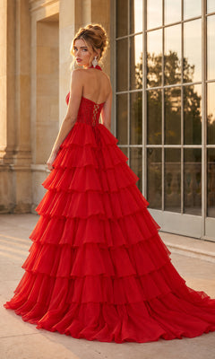 A woman in the Halter Prom Ball Gown: PromGirl Exclusive 250352 stands outdoors, looking over her shoulder, with large windows and stone columns in the background.