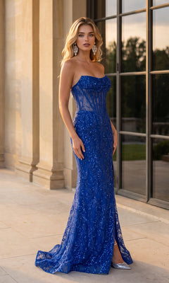 A woman wearing the Glitter Corset Prom Dress: PromGirl 250362—a strapless, floor-length blue sequin gown—stands on a stone patio in front of tall windows and columns, looking at the camera.