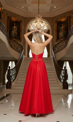 A woman wearing the Poly USA 25036 long prom dress with an a-line mesh skirt stands at the base of a grand staircase, facing away, hands raised to her head in an elegant interior with chandeliers and portraits.