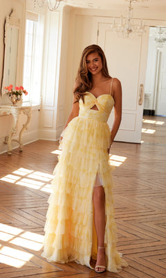 A woman smiles at the camera in a bright room, wearing the Long Yellow Ruffled Prom Dress: Juliet JT2508A, featuring spaghetti straps, a high slit, and a tiered A-line skirt.