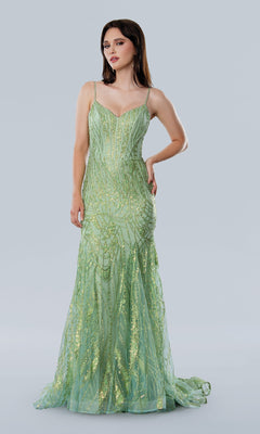 A woman wears the Stella Couture 25105, a floor-length light green prom dress with thin straps, a corset bodice, and gold sequin details, standing against a plain gray background.