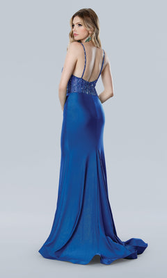 A woman faces away, wearing the Stella Couture 25164 long prom dress in royal blue with a beaded sheer bodice and fitted mermaid silhouette, set against a plain light gray background.