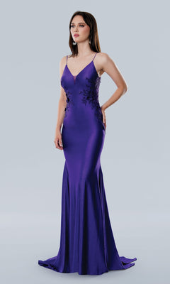 A woman stands in the Stella Couture 25186, a fitted floor-length purple prom dress with a v-neckline and floral lace on the bodice and sides, set against a plain light gray background.