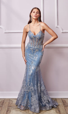 A woman poses against a decorative white wall wearing the Aerie Couture 251, a long glitter-print prom dress with a fitted mermaid silhouette, light blue color, silver floral embroidery, and thin straps.