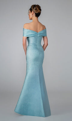 A woman in the Stella Couture 25329 long formal dress—an off-the-shoulder, fitted, light blue mermaid gown with a subtle sheen—stands with her back to the camera against a plain grey backdrop.