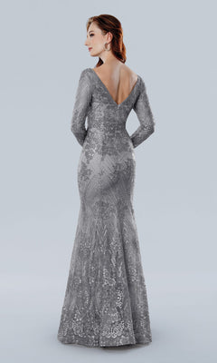 A woman faces away, wearing the Stella Couture 25332 long formal dress in silver—a floor-length gown with sheer sleeves, a V-shaped back, and intricate lace detailing.