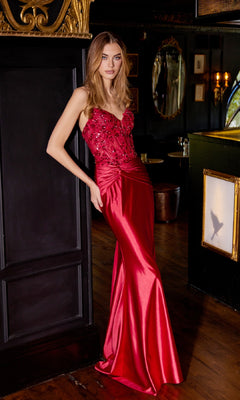 A woman stands indoors by a dark wall with ornate gold trim, wearing the Sequin-Bodice Long Prom Dress: Juliet JT2534K, featuring a strapless design and embellished corset bodice.