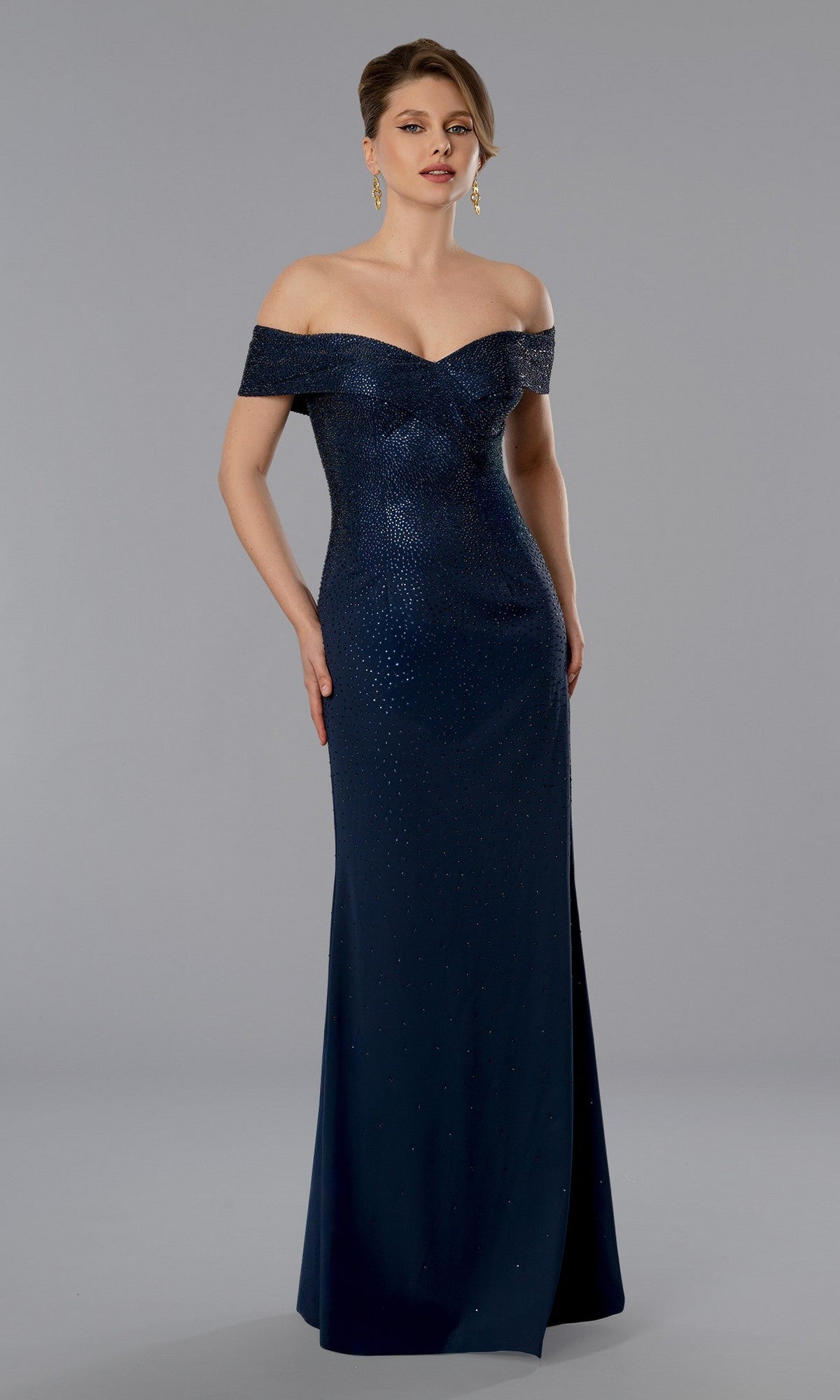 A woman in the Stella Couture 25357 long formal dress in navy, featuring an off-the-shoulder sweetheart neckline, stands against a plain gray background.