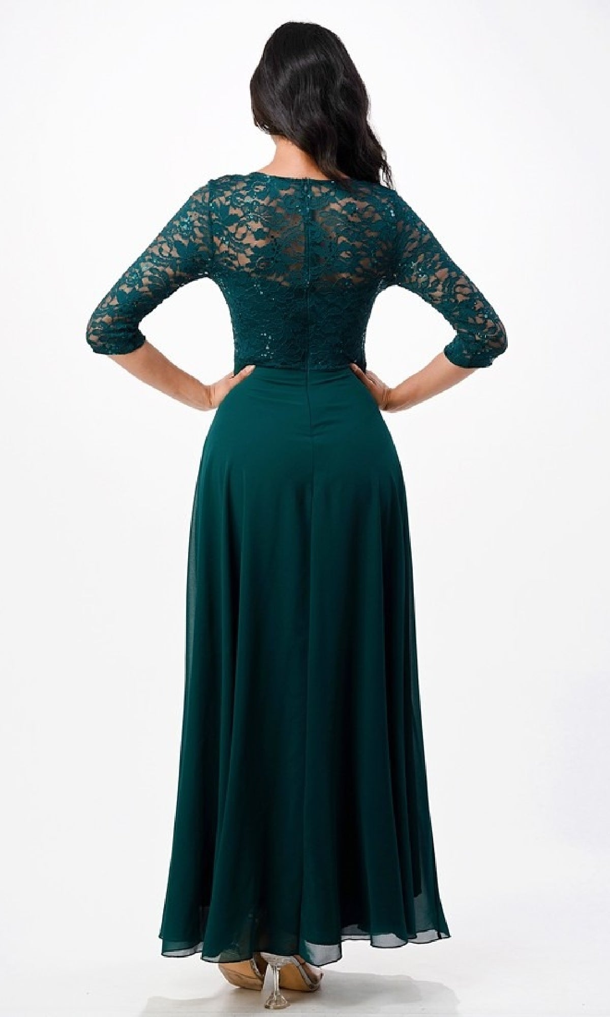 A woman faces away from the camera in a Plus-Size A-Line Long Formal Dress with Sleeves—dark green, floor-length, with lace sleeves and upper back—paired with beige shoes, set against a plain white background.