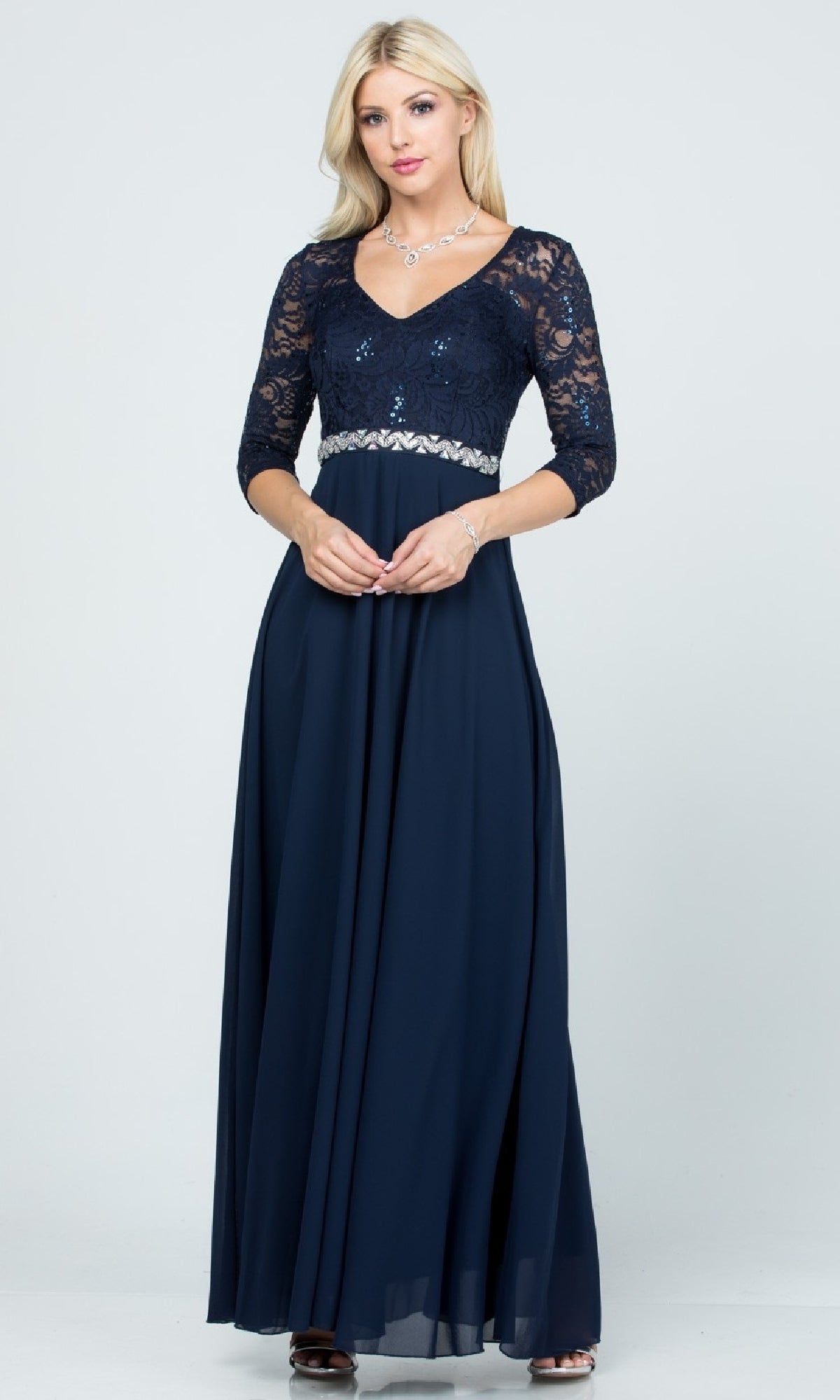 A woman models the Plus-Size A-Line Long Formal Dress with Sleeves—a navy blue gown with an a-line skirt, lace sleeves, sequin v-neck bodice, and waistband. She has blonde hair and wears jewelry.