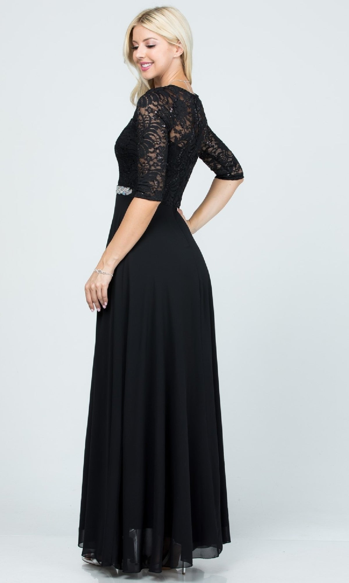Woman in the Sleeved V-Neck Long A-Line Formal Dress 25434, a floor-length black sequin-lace gown with lace half sleeves and a fitted bodice, stands sideways and smiles against a plain background.