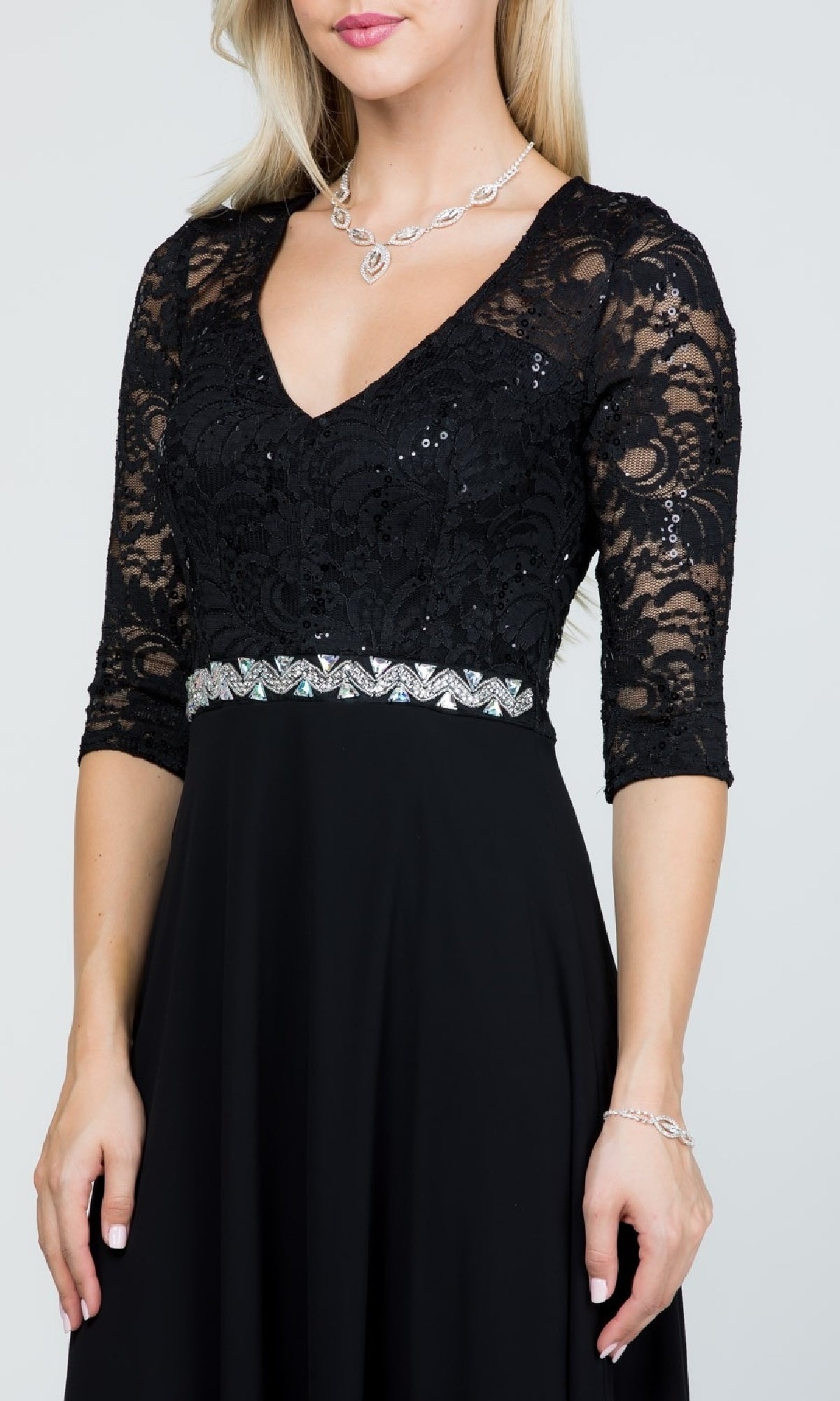 A woman models the Sleeved V-Neck Long A-Line Formal Dress 25434, featuring black lace sleeves, a rhinestone waistline, and an elegant chiffon skirt, styled with silver jewelry against a plain background.