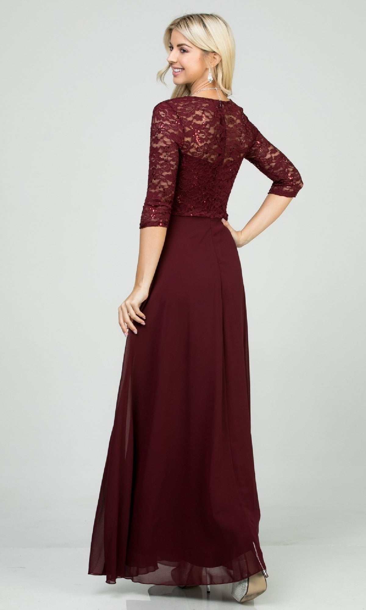 A woman wearing the Sleeved V-Neck Long A-Line Formal Dress 25434, featuring three-quarter sleeves and a flowing burgundy chiffon skirt, stands facing away and looks over her shoulder.