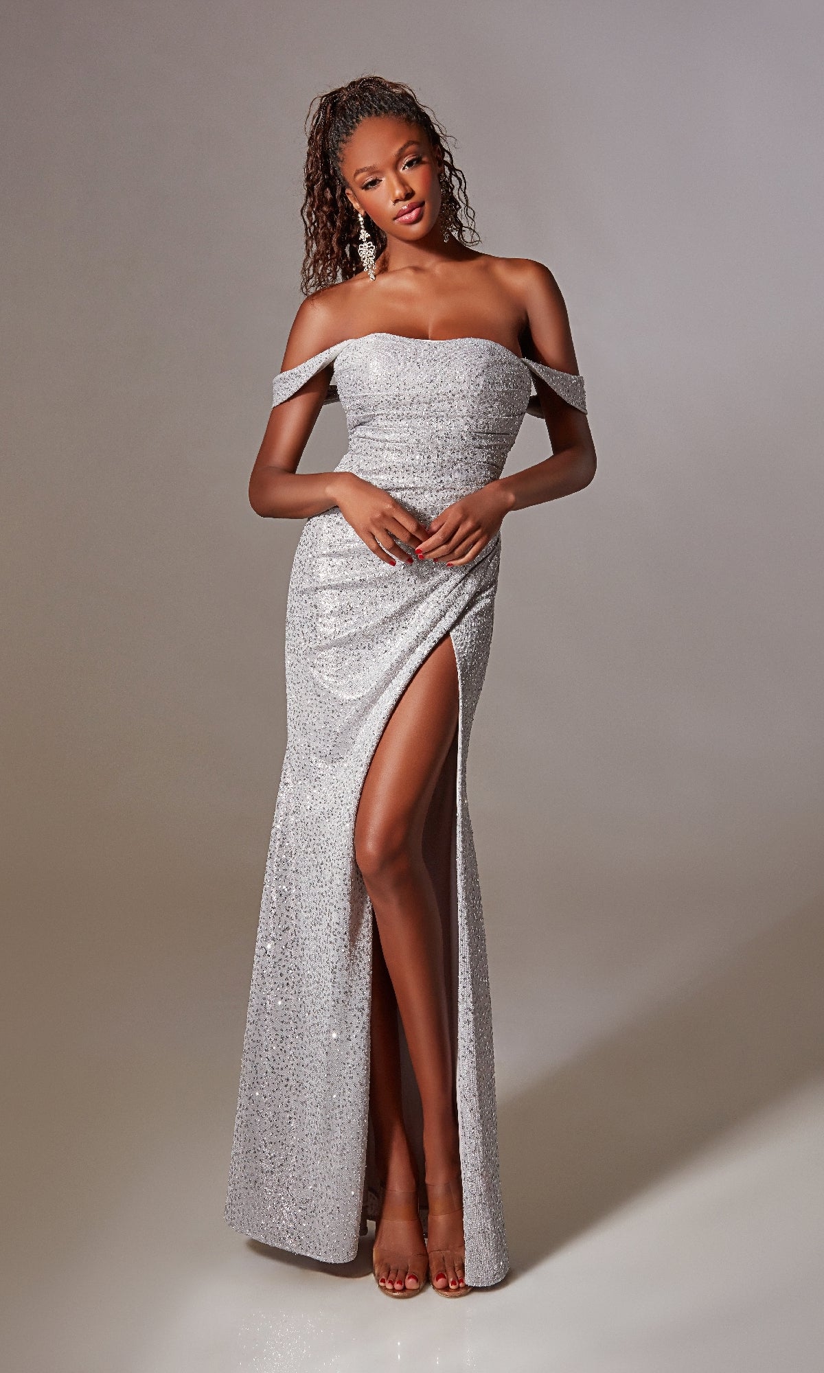 A woman poses gracefully against a plain background, wearing the Lace-Up Long Sequin Prom Dress: Aerie Couture 254—a silver off-the-shoulder gown with a thigh-high slit.