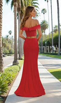 Woman in a red off-shoulder evening gown standing on a sidewalk with palm trees in the background.