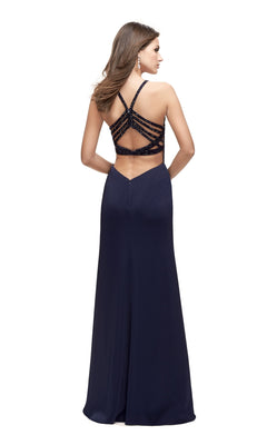 A woman wearing the La Femme 25669 Long Prom Dress, a floor-length navy blue gown with an open back and multiple crisscrossing beaded straps, stands against a white background.