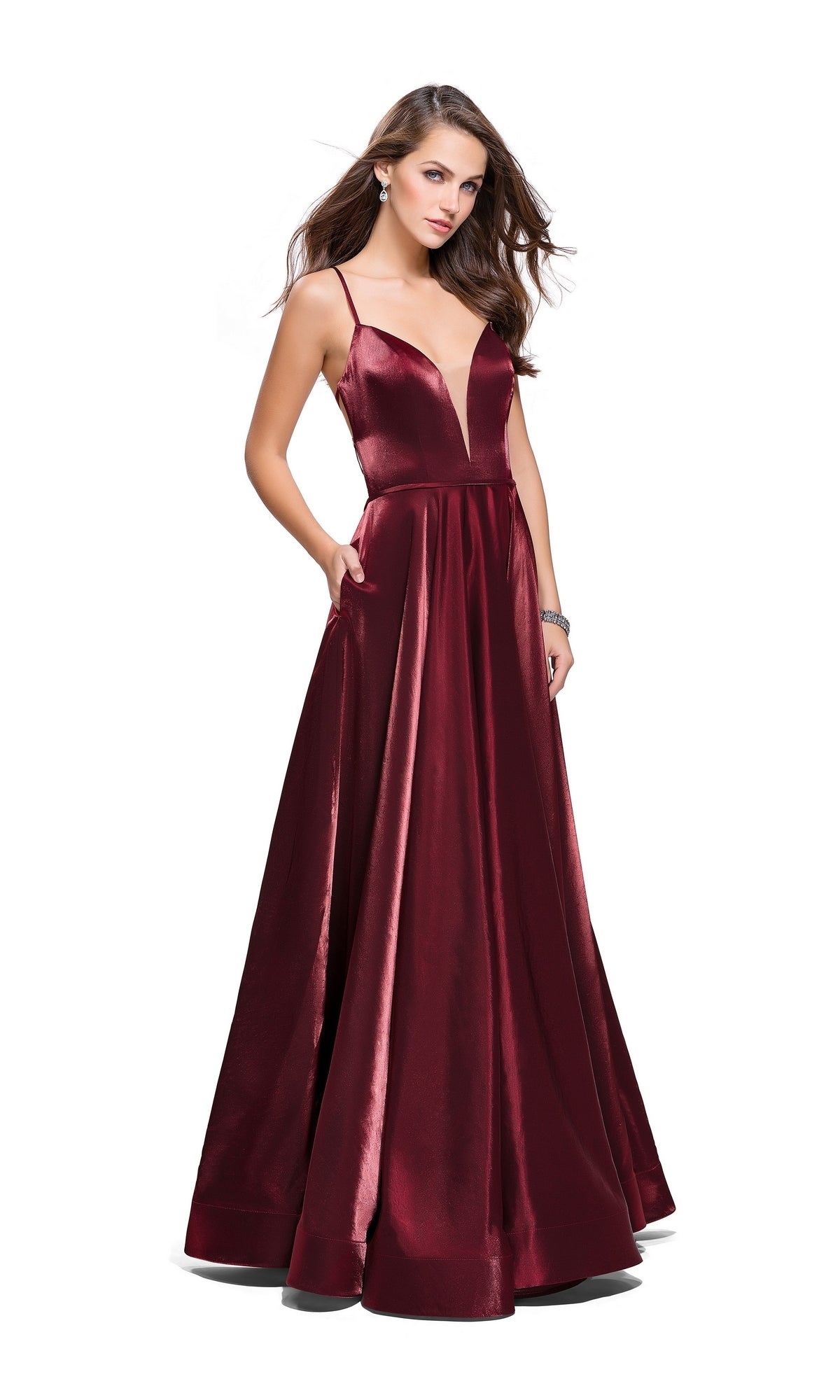 A woman stands against a white background in a sleeveless, floor-length La Femme 25670 Long Prom Dress featuring burgundy satin, a deep V-neckline, thin straps, and an open back.