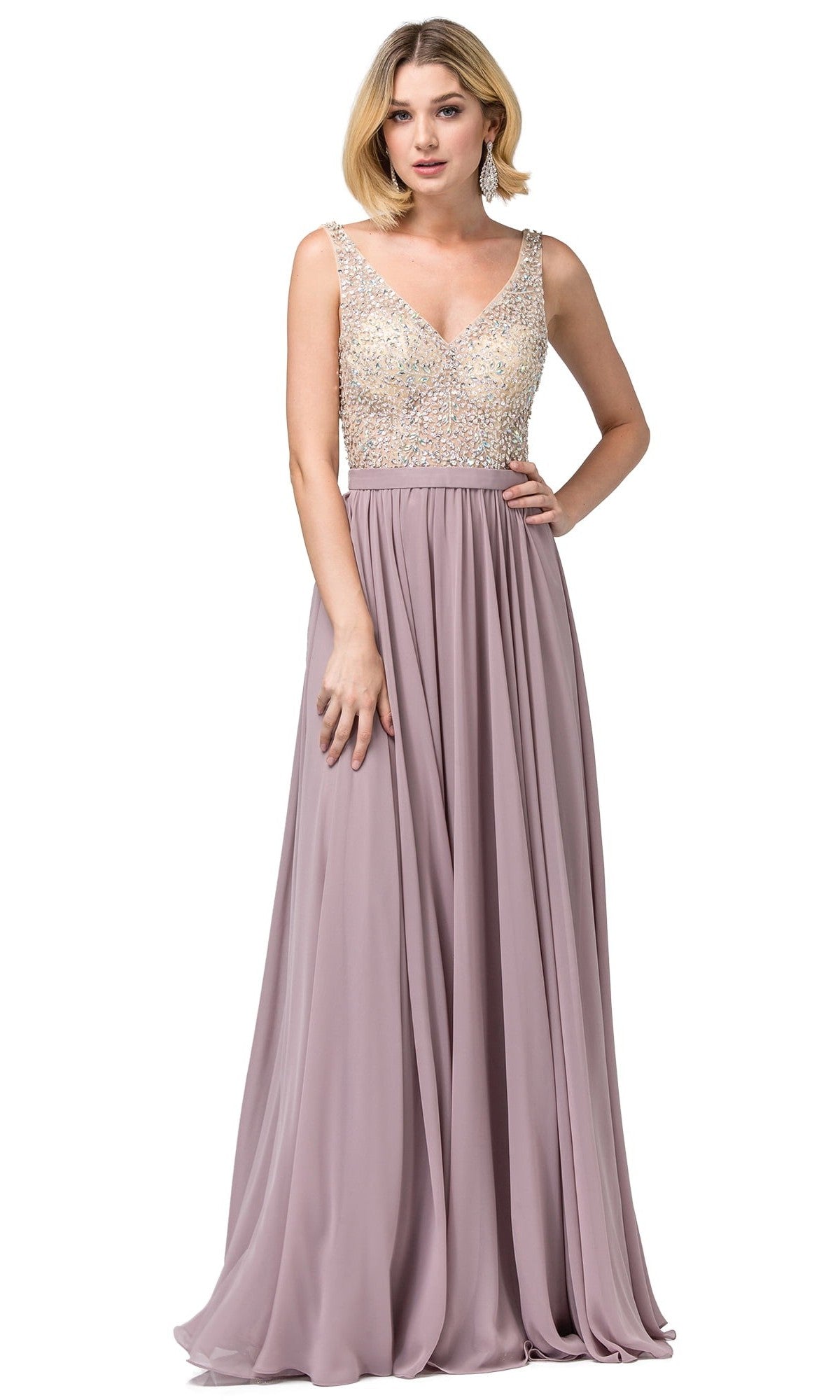 A woman wearing a sleeveless, floor-length mocha Long Illusion-Beaded-Bodice V-Neck Prom Dress with a beaded bodice and a flowing chiffon skirt stands with one hand resting on the skirt.