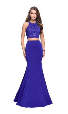A woman models the La Femme 25759 Long Prom Dress, a two-piece set with a sleeveless royal blue lace crop top and a floor-length flared skirt, against a white background.