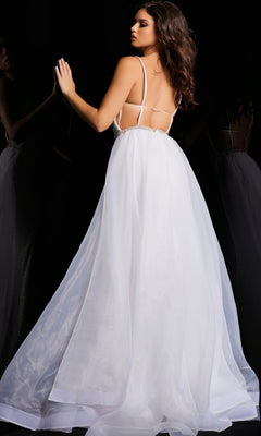 A woman in the Jovani Tulle-Overskirt Beaded-Net Prom Dress 25990, featuring a white backless design with thin straps, stands against a dark background, her hand touching a reflective surface.