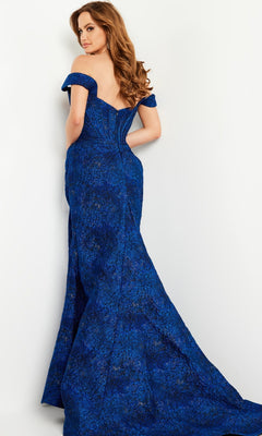 A woman poses against a white backdrop, looking over her shoulder in the Jovani 26017 Cobalt Blue Long Formal Dress, an off-the-shoulder floor-length gown with a striking textured pattern.