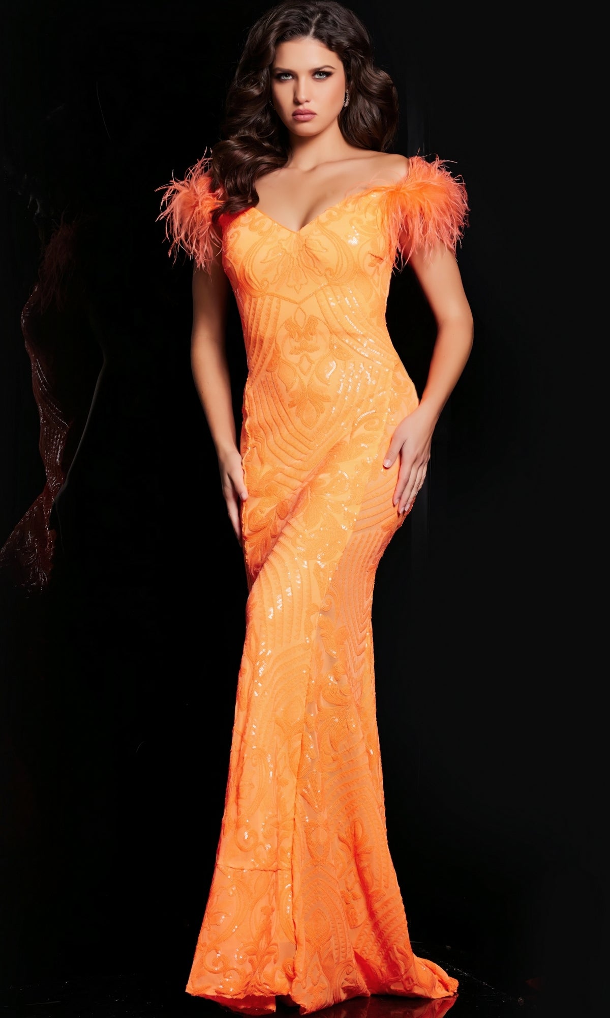 A woman stands against a black background wearing the Jovani Feathered Long Sequin Prom Dress 26041—fitted, floor-length, bright orange with off-the-shoulder feathered sleeves.