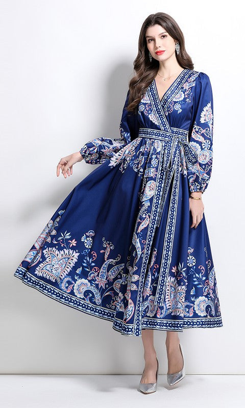 A woman poses against a white background wearing the A-Line Long-Sleeve Print Casual Maxi Wrap Dress in Navy Multi, featuring intricate white and pastel floral patterns. This ankle-length summer dress is paired with elegant silver heels.