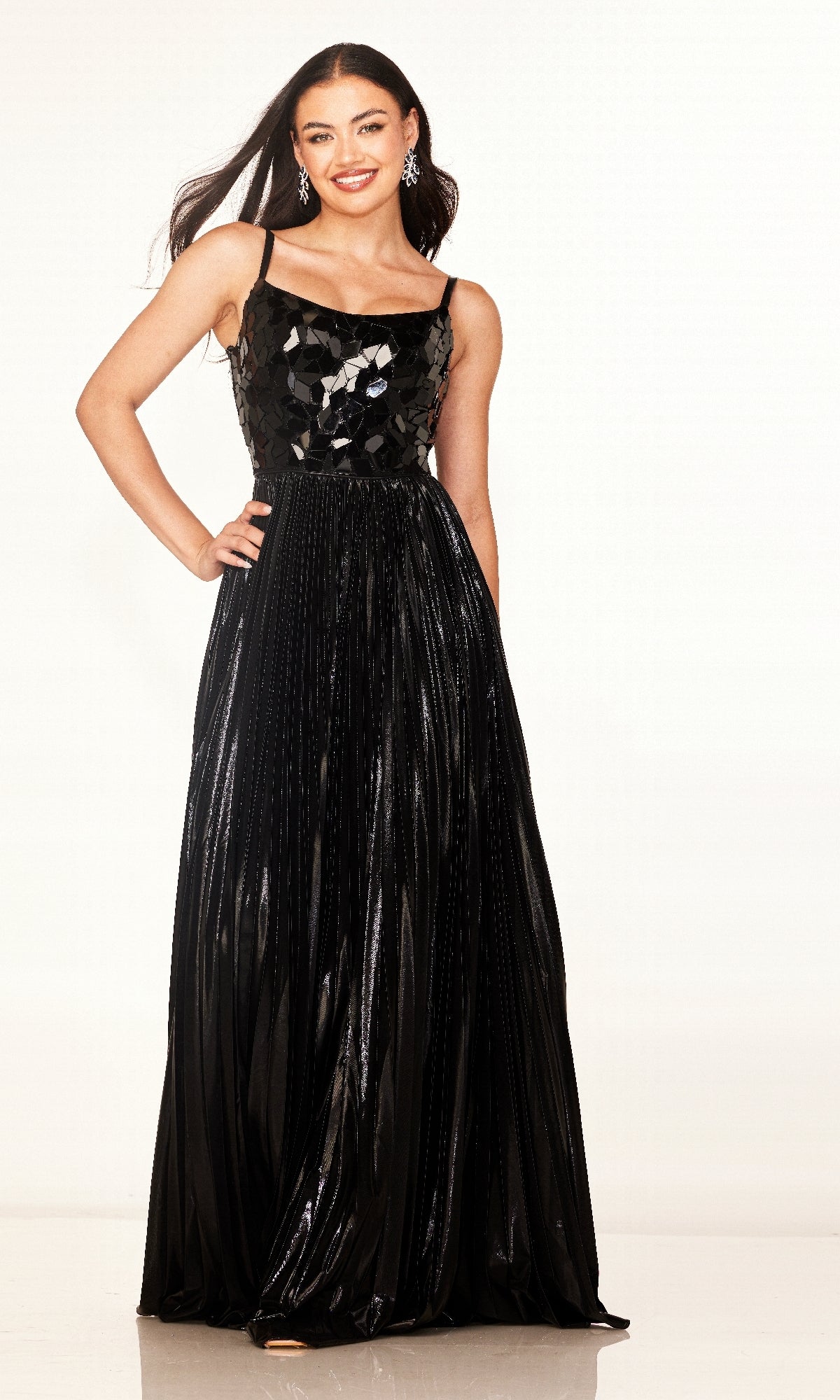A woman stands smiling against a plain background wearing the Cecilia Couture 2609, a long black sleeveless A-line prom dress with a glossy embellished bodice and pleated skirt.