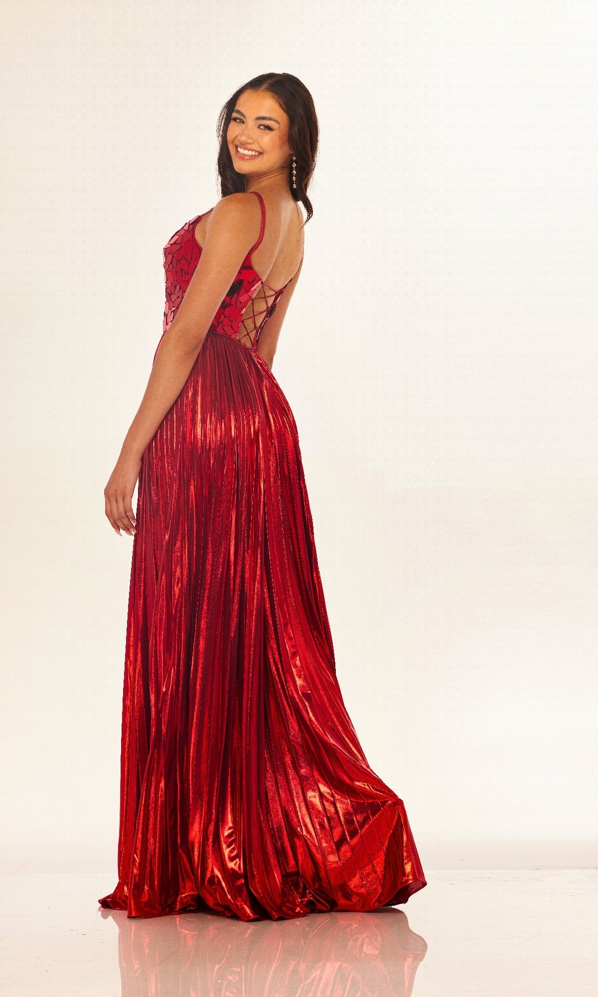 A woman smiles over her shoulder in the Long Prom Dress: Cecilia Couture 2609, a sleeveless, shiny red gown with a lace-up back, posing against a light background.