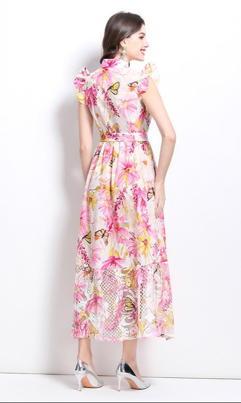 A woman faces away, wearing a High-Neck Long Print Casual Dress with Cap Sleeves in floral patterns, paired with silver high-heeled shoes against a plain white background.