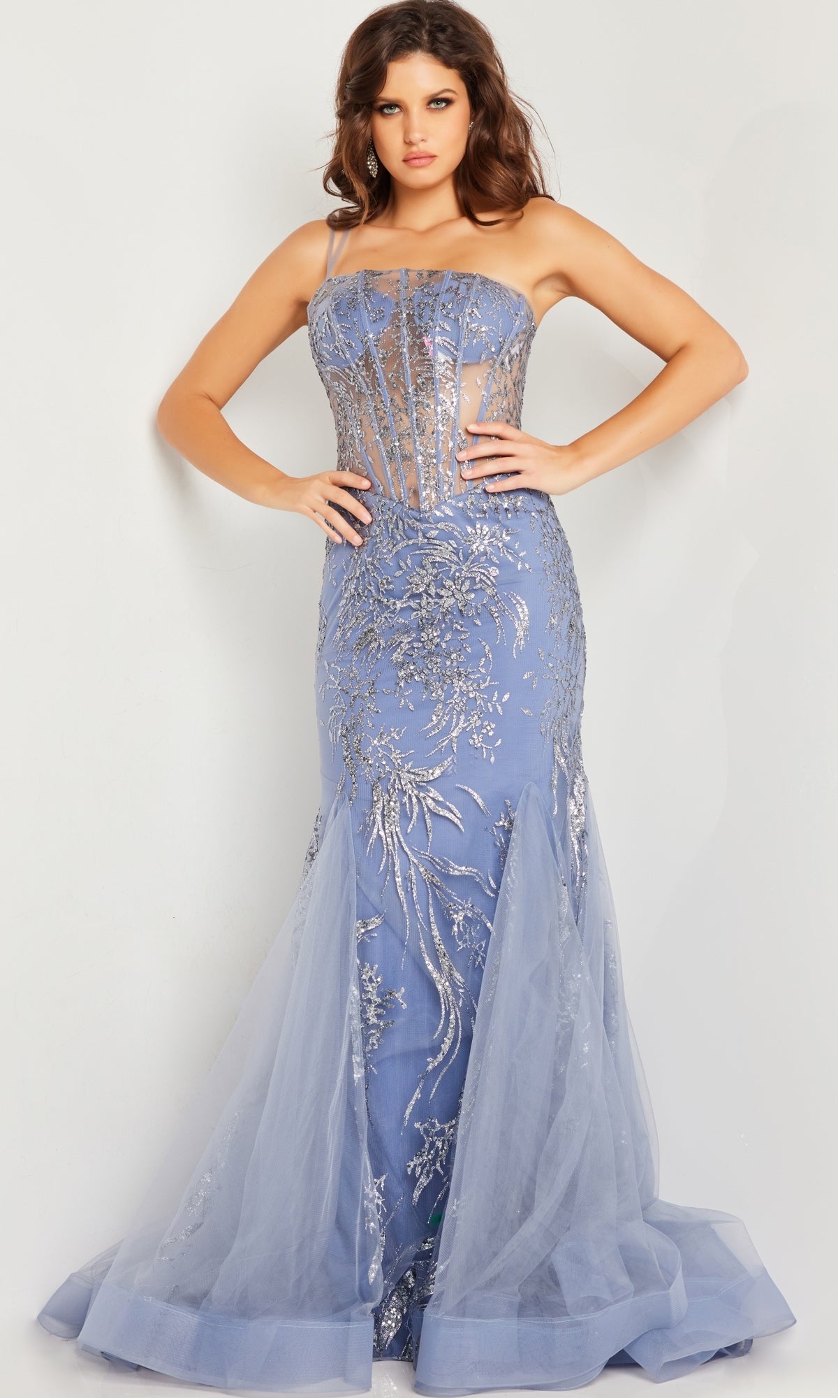 A woman wears the Jovani Sheer-Waist Long Glitter Prom Dress 26112, featuring a fitted strapless design with silver embellishments, sheer bodice details, and tulle accents at the hem.