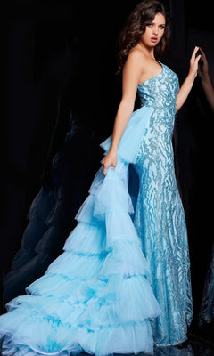 A woman wears the Jovani Ruffled Long Glitter-Print Prom Dress 26119 in icy blue, featuring a fitted silhouette and dramatic tiered tulle train, standing against a dark background.