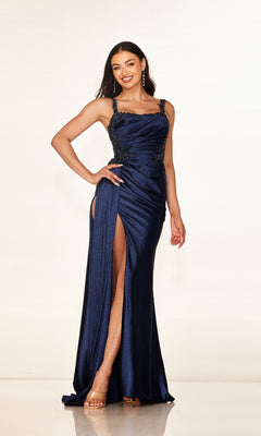 A woman smiles against a plain background wearing the Cecilia Couture 2612 long prom dress, a navy blue, form-fitting gown with beaded straps, side embellishments, and a high leg slit.