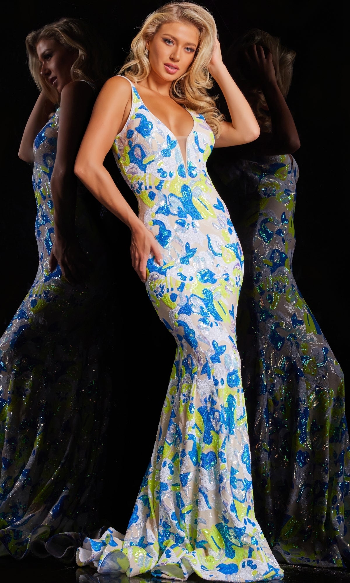 A woman poses in the Jovani V-Back Long Sequin-Print Prom Dress 26130, a fitted sleeveless gown with a plunging neckline and vibrant blue, green, and white sequined print, her reflection visible against a dark background.