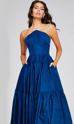 A woman poses confidently with hands in the pockets of the Jovani 26152 long formal dress, a strapless taffeta evening gown featuring a textured blue finish, fitted bodice, and full skirt.