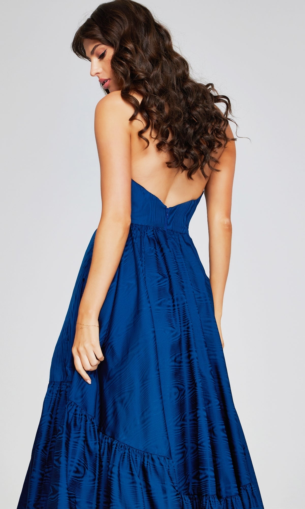 Woman with long wavy hair, shown from the back against a light background, wearing the Jovani 26152 long formal dress—strapless, blue textured taffeta evening gown.