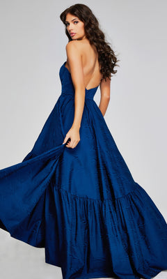 A woman with wavy brown hair wears the Jovani 26152 long formal strapless taffeta evening gown in dark blue, featuring a low back, standing against a plain light background.