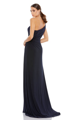 A woman poses with her back turned, looking over her shoulder, showcasing the navy blue Mac Duggal 26163 one-shoulder long formal dress against a white background.