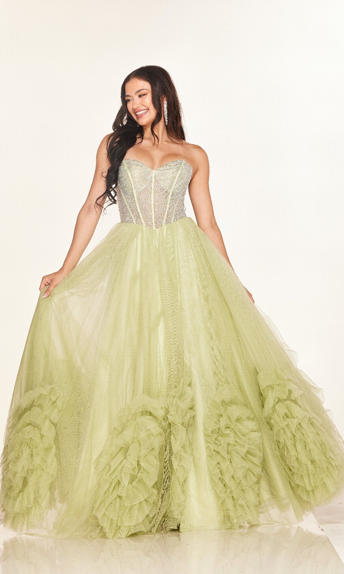 A woman smiles against a plain background wearing the Long Prom Dress: Cecilia Couture 2617—a strapless, light green gown with a rhinestone corset bodice and full ruffled A-line tulle skirt.